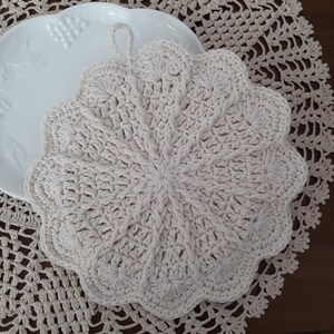May include: A crocheted pot holder in a cream color with a scalloped edge and a loop for hanging.