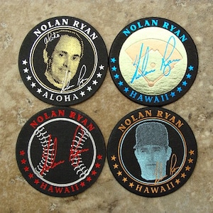 May include: Four black round coasters with a white border and a gold, silver, or red design. Each coaster features a different image of baseball player Nolan Ryan, including a portrait, a baseball, and a signature. The text "NOLAN RYAN" and "HAWAII" are printed on each coaster.