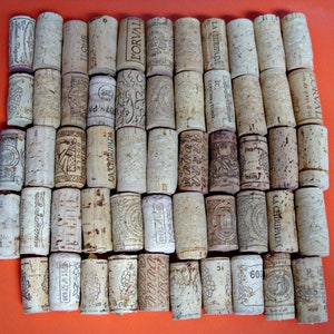 May include: A collection of 40 wine corks arranged in a rectangular pattern. The corks are made of natural cork and have various labels and markings. Some of the labels include the words "L'ORVAL", "LA CHIRIPADA", and "BOGLE".