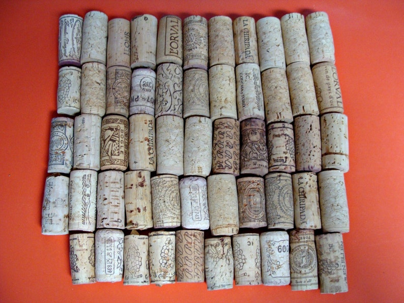 May include: A collection of 40 wine corks arranged in a rectangular pattern. The corks are made of natural cork and have various labels and markings. Some of the labels include the words "L'ORVAL", "LA CHIRIPADA", and "BOGLE".