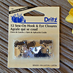 May include: A package of 12 sew-on hook and eye closures in brass. The package is labeled "Dritz" and "Bonus Pack!" with the text "12 Sew-On Hook & Eye Closures" and "Agrafe qui se coud".