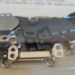 May include: A close-up of a package of silver-toned metal hook and eye closures. The closures are packaged in a clear plastic container.