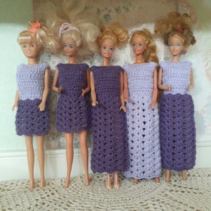 May include: Five purple crochet dresses for dolls. The dresses are all different styles and have a lacy pattern.