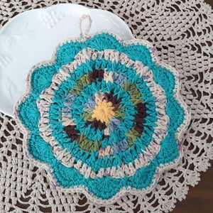 May include: A crocheted teal and beige hot pad with a multi-colored center. The hot pad has a loop for hanging.