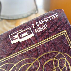 May include: Close-up of a burgundy box with gold trim and text. The box features the words "2 CASSETTES" and the number "40600" in white. A white graphic of two cassette tapes is also visible.