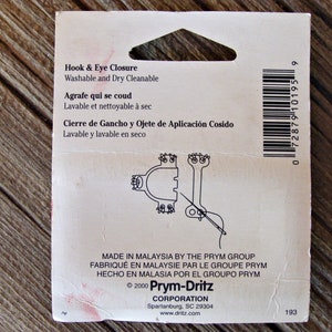 May include: A white package with black text and a barcode. The text reads "Hook & Eye Closure Washable and Dry Cleanable Agrafe qui se coud Lavable et nettoyable &agrave; sec Cierre de Gancho y Ojete de Aplicaci&oacute;n Cosido Lavable y lavable en seco Made in Malaysia by the Prym Group Fabriqu&eacute; en Malaysie par le Groupe Prym Hecho en Malasia por el Grupo Prym &copy; 2000 Prym-Dritz Corporation Spartanburg, SC 29304 www.dritz.com 193".