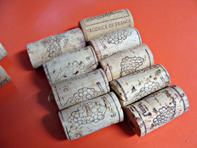 May include: A close-up of a group of cork wine bottle stoppers with a grape design and the text "PRODUCE OF FRANCE".