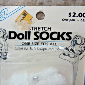 May include: A package of white stretch doll socks for soft sculptured dolls. The package has a picture of a doll wearing the socks and the text "Stretch Doll Socks, One Size Fits All, Great for Soft Sculptured Dolls, $2.00 One pair - 635".