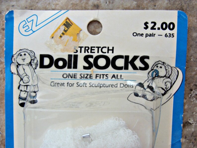 May include: A package of white stretch doll socks for soft sculptured dolls. The package has a picture of a doll wearing the socks and the text "Stretch Doll Socks, One Size Fits All, Great for Soft Sculptured Dolls, $2.00 One pair - 635".
