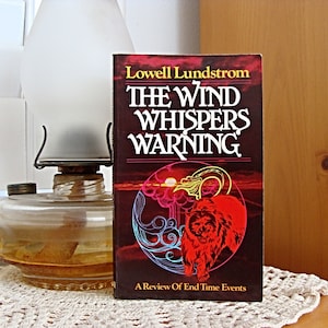 May include: A book titled "The Wind Whispers Warning" by Lowell Lundstrom. The cover features a red lion with a sunset and swirling clouds in the background. The book is about a review of end time events.