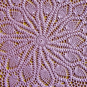 May include: A close-up of a purple crocheted doily with a circular pattern. The doily is made with delicate stitches and has a lacy appearance.
