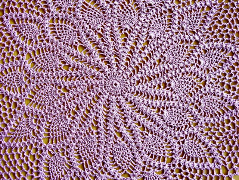 May include: A close-up of a purple crocheted doily with a circular pattern. The doily is made with delicate stitches and has a lacy appearance.