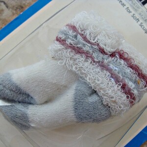 May include: White and gray doll socks with a red and gray trim. The socks are made of a soft, fuzzy material. The packaging says "Size Fits All" and "Great for Soft Sculptured Dolls".