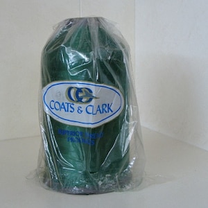 May include: A spool of green thread wrapped in clear plastic packaging. The label reads "Coats & Clark Superior Thread Products."