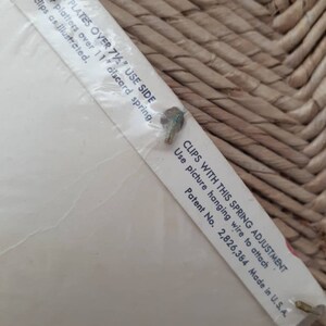 May include: Close-up of a white label with instructions for using picture hanging clips. The label reads "FOR PLATES OVER 7 1/2" USE SIDE" and "CLIPS WITH THIS SPRING ADJUSTMENT. Use picture hanging wire to attach. Patent No. 2,826,384 Made in U.S.A."