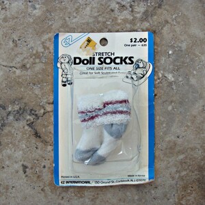 May include: A package of white and gray stretch doll socks with red trim. The package is labeled "Stretch Doll Socks" and "One Size Fits All". The price is $2.00.