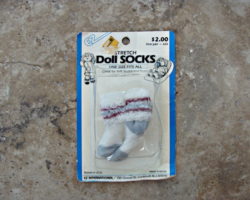May include: A package of white and gray stretch doll socks with red trim. The package is labeled "Stretch Doll Socks" and "One Size Fits All". The price is $2.00.