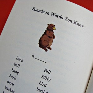 Może przedstawiać: Otwarta strona książki z tytułem "Sounds in Words You Know". Ilustracja brązowego niedźwiedzia znajduje się nad listą sł&oacute;w zaczynających się na literę "b". Słowa obejmują "back", "ball" i "bang".