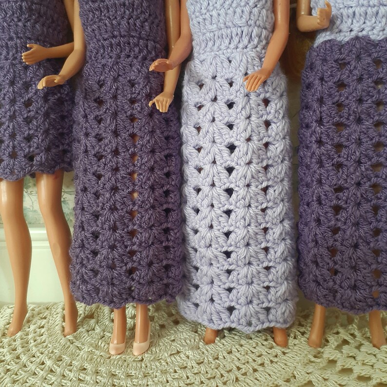 May include: Four crocheted dresses in shades of purple and lavender. The dresses are made with a delicate stitch pattern and have a flowing, feminine silhouette.