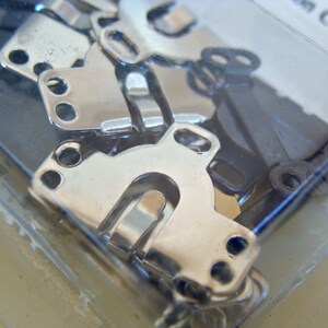 May include: A close-up of a package of silver metal clasps. The clasps are in various shapes and sizes, and they are all shiny and new.