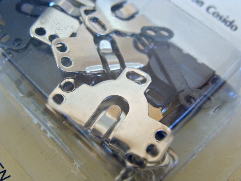 May include: A close-up of a package of silver metal clasps. The clasps are in various shapes and sizes, and they are all shiny and new.
