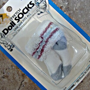 May include: A package of white doll socks with gray and pink stripes. The package is labeled "Stretch Doll Socks" and "One Size Fits All".
