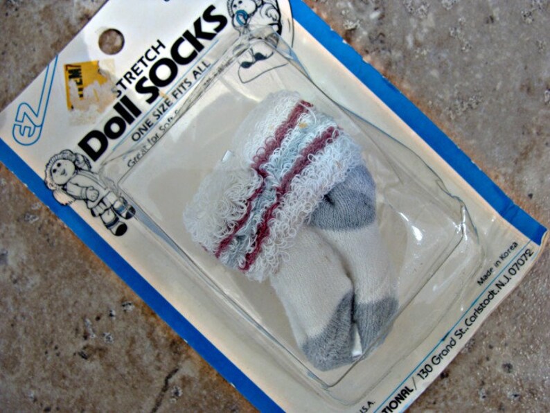 May include: A package of white doll socks with gray and pink stripes. The package is labeled "Stretch Doll Socks" and "One Size Fits All".