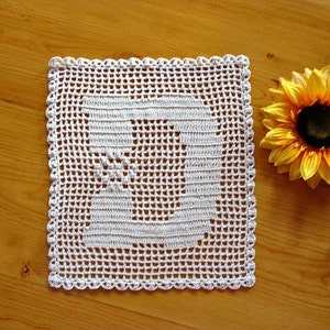 May include: White crocheted doily with a square design. The doily is on a wooden surface with a yellow sunflower.