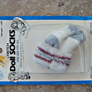 May include: A package of white and blue doll socks with red stripes. The package is blue and white and says "Stretch Doll Socks" and "One Size Fits All".
