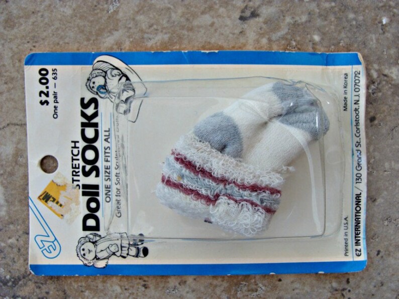 May include: A package of white and blue doll socks with red stripes. The package is blue and white and says "Stretch Doll Socks" and "One Size Fits All".