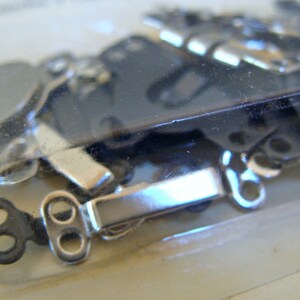 May include: A close-up of a package of silver and black metal clasps. The clasps are designed to be used for attaching fabric or other materials together.