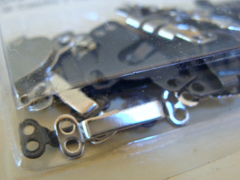 May include: A close-up of a package of silver and black metal clasps. The clasps are designed to be used for attaching fabric or other materials together.