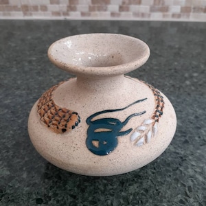 May include: A small, beige ceramic vase with a textured surface. The vase has a wide mouth and a narrow neck. It is decorated with brown, white, and green painted designs.
