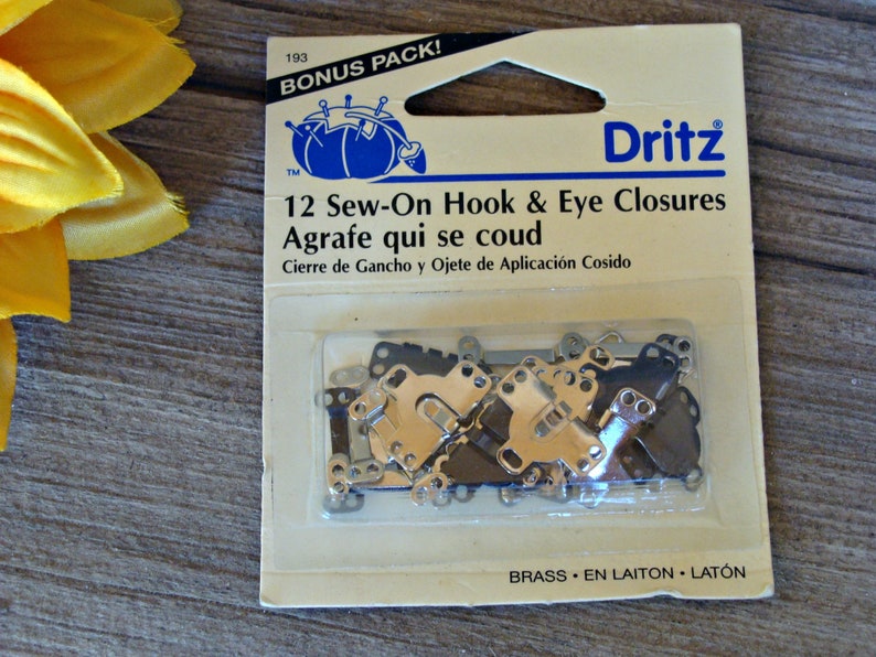 May include: A package of 12 sew-on hook and eye closures in brass. The package is labeled "Dritz" and says "12 Sew-On Hook & Eye Closures" and "Agrafe qui se coud".