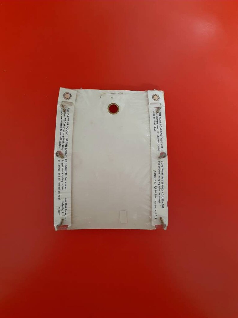 May include: White plastic plate hanger with a spring adjustment for plates up to 7 1/4 inches. The hanger has a hole in the center and a small white label with instructions for use. Patent No. 2,826,384 Made in U.S.A.
