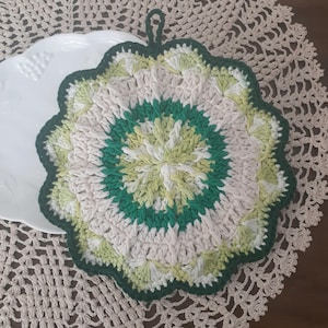 May include: A crocheted pot holder with a green, white, and yellow design. The pot holder has a loop for hanging.