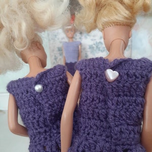 May include: Two purple crocheted tops with different embellishments. One top has a pearl button and the other has a heart-shaped button.
