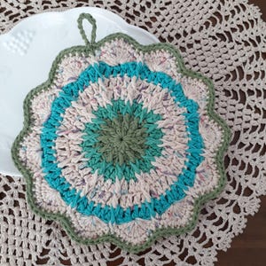 May include: A crocheted pot holder with a green, blue, and pink color scheme. The pot holder has a scalloped edge and a loop for hanging.