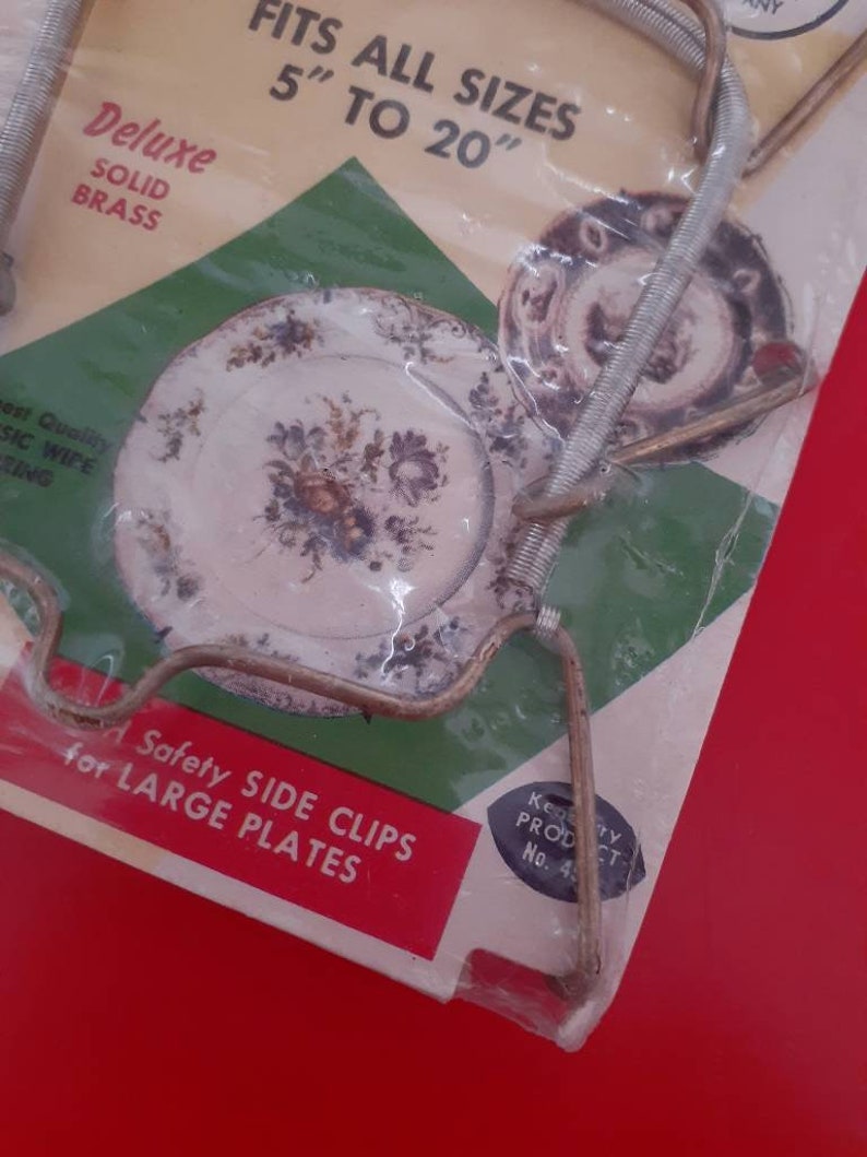 May include: A package of two brass plate clips for holding large plates. The package says "Fits all sizes 5" to 20" Deluxe Solid Brass" and "Safety Side Clips for Large Plates".