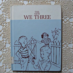 Może przedstawiać: Vintage książka zatytułowana "The New We Three" z jasnoniebieską okładką. Okładka zawiera ilustracje dzieci w pobliżu drewnianego płotu, narysowane brązowym tuszem.