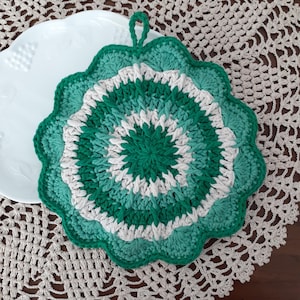 May include: A green and white crocheted pot holder with a loop handle. The pot holder is round and has a scalloped edge.