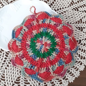 May include: A colorful crocheted pot holder with a scalloped edge and a loop handle. The pot holder is made with red, green, blue, and pink yarn.