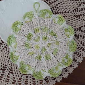 May include: A crocheted pot holder with a green and white pattern. The pot holder has a loop for hanging.