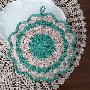 May include: A crocheted pot holder in a teal and cream color scheme with a scalloped edge and a loop for hanging.