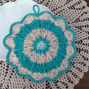 May include: A teal and cream crocheted pot holder with a scalloped edge and a loop handle.