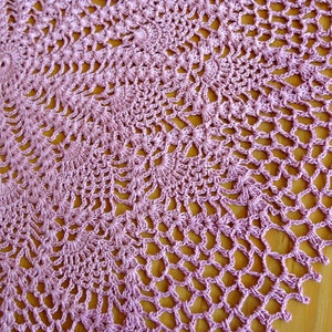 May include: A delicate, round, crocheted doily in a pale lavender color. The doily is made with a fine thread and has a delicate, intricate pattern.
