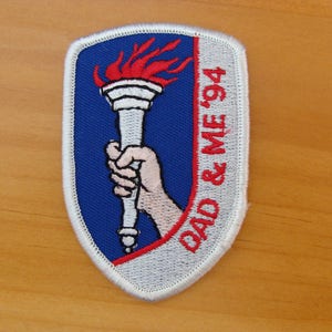 May include: A white and blue embroidered patch with a red torch and the text "DAD & ME '94".