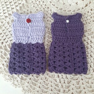 May include: Two crocheted dresses, one in lavender and purple and the other in purple. Both dresses have a sleeveless bodice and a flared skirt.