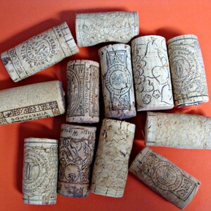 May include: A collection of 11 cork bottle stoppers with various designs and labels. The stoppers are made of natural cork and have a variety of colors and patterns. Some of the stoppers have text on them, including "VINEYARDS" and "WINE CELLARS".