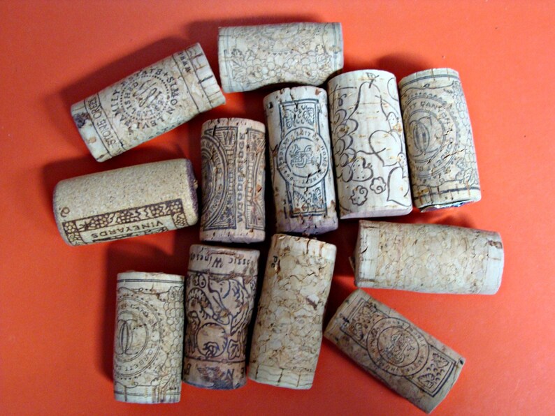 May include: A collection of 11 cork bottle stoppers with various designs and labels. The stoppers are made of natural cork and have a variety of colors and patterns. Some of the stoppers have text on them, including "VINEYARDS" and "WINE CELLARS".